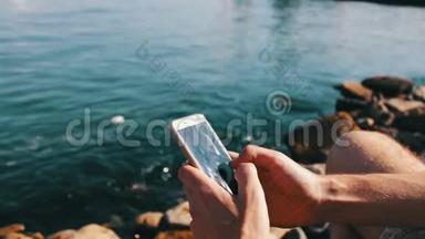 一个年轻人的手在里海的海浪背景下，在智能手机上键入一些东西